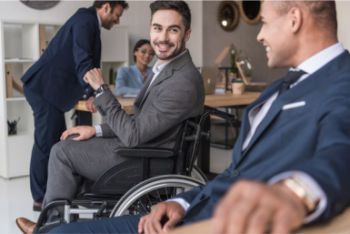 Two colleagues smiling and talking, one is in a wheelchair