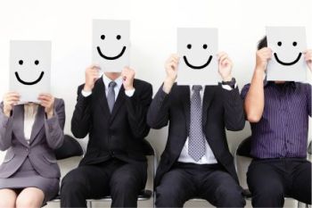 Office workers holding up signs in front of their faces with smiley faces on them