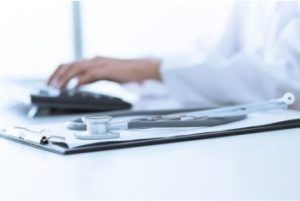 Close up of a woman typing up medical notes, a stethoscope is by the keyboard