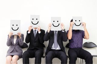 Group of workers holding signs in front of their faces that have smiley faces on them