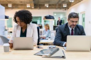 Colleagues working in an office using their mobile phones, both have laptops in front of them