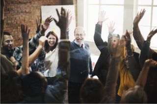 Employees enthusiastically giving a show of hands to volunteer for a cause.