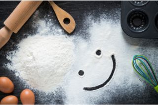 Baking utensils, eggs and flour. A smiley face is drawn in the flour.