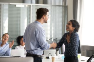Manager congratulating an employee, his hand is reaching our for hers and she is laughing.
