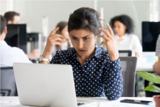 Worker sat in front of a laptop looking stressed.